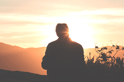 Man is reflecting on growth and gratitude while looking at sunset