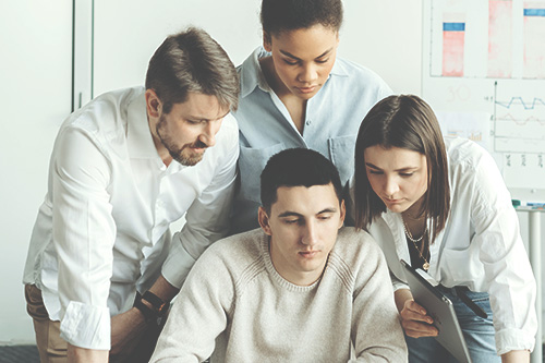 A group of people looks tense as they stand around the computer working on the top 6 ideas for conflict resolution