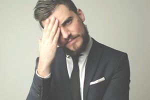Man holding his head looking frustrated about how to go from manager to leader to grow your business