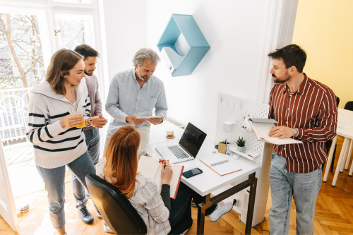 The image shows a group of five people engaged in a collaborative discussion in a bright, modern office setting.